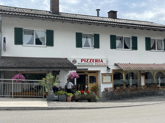 Pizzeria Ristorante Vesuvio - Außenansicht Ein Wohnhaus mit einer Pizzeria im Erdgeschoss. Sitzmöglichkeiten vor dem Haus. Bunte Blumenkästen wirken einladend.