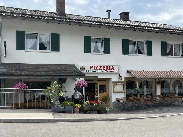 Pizzeria Ristorante Vesuvio - Außenansicht Ein Wohnhaus mit einer Pizzeria im Erdgeschoss. Sitzmöglichkeiten vor dem Haus. Bunte Blumenkästen wirken einladend.