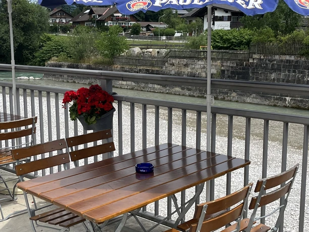 Pizzeria Restaurante Vesuvio - Außensitzbereich an der Loisach Holztisch mit vier Stühlen unter einem Sonnenschirm direkt an der Loisach