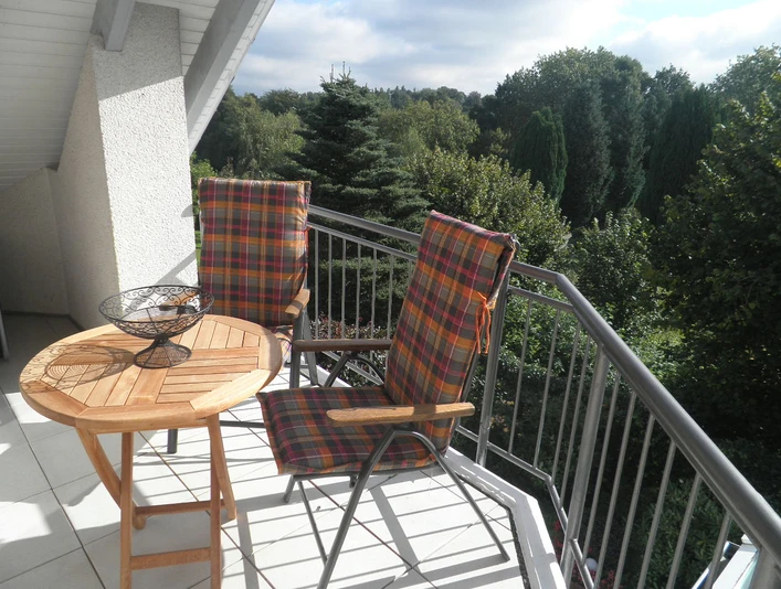 Toller Blick vom Balkon Zwei bunte Stühle und ein runder Holztisch auf einem Balkon mit grünem Ausblick in einen Wald.