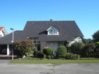 Außenansicht Ein modernes Einfamilienhaus mit dunklem Giebeldach und gepflegtem Vorgarten an einem sonnigen Tag.