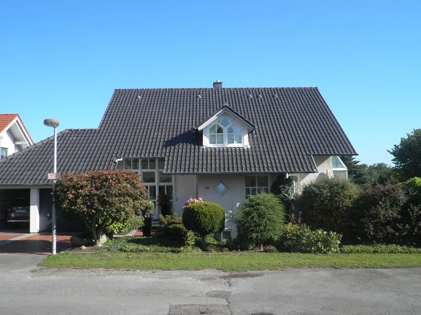 Außenansicht Ein modernes Einfamilienhaus mit dunklem Giebeldach und gepflegtem Vorgarten an einem sonnigen Tag.