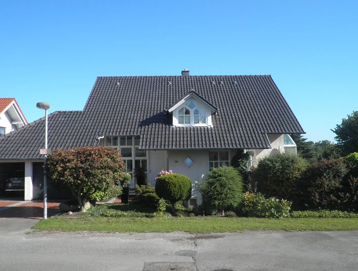 Außenansicht Ein modernes Einfamilienhaus mit dunklem Giebeldach und gepflegtem Vorgarten an einem sonnigen Tag.