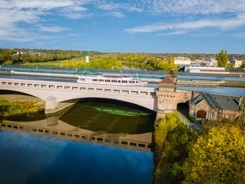 Minden-Wasserstraßenkreuz-Teutoburger-Wald-Tourismus-J-Motzny-002.jpg Eine historische Brücke in Minden mit vorbeifahrendem Ausflugsschiff über einem Fluss, umgeben von Herbstlandschaft.