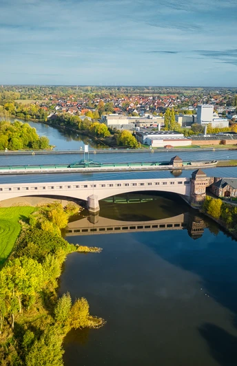 Luftaufnahme der Schachtschleuse Minden, umgeben von Flusslandschaft und grüner Vegetation im Herbst.