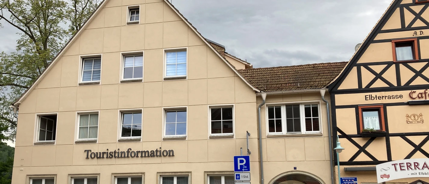 Touristinformation am Markt in Stadt Wehlen Zweistöckiges Gebäude mit der Aufschrift "Touristinformation", daneben Fachwerkhaus mit Restaurant "Elbterrasse", bewölkter Himmel.
