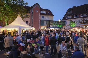 Menschen genießen das Vlothoer Weinfest 2023 im Freien mit Lichterketten und Verkaufsständen.