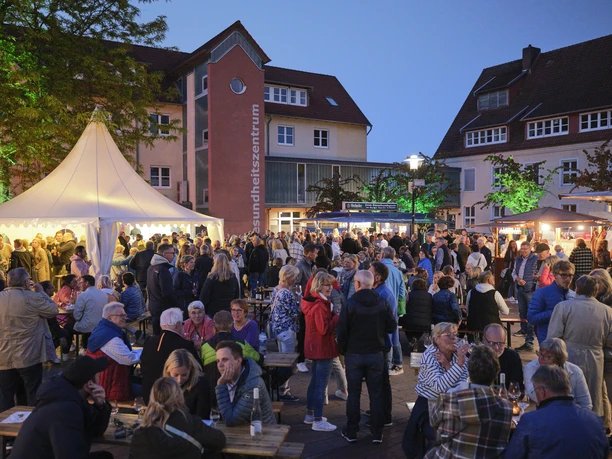 Menschen genießen das Vlothoer Weinfest 2023 im Freien mit Lichterketten und Verkaufsständen.