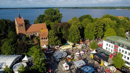 bad-zwischenahner-woche-von-oben-marktgelaende.jpg Luftaufnahme eines belebten Marktgeländes in Bad Zwischenahn mit Kirche im Hintergrund und See im Westen.