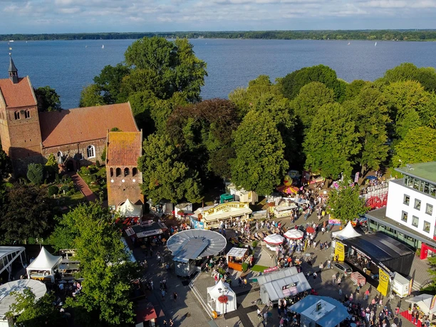 bad-zwischenahner-woche-von-oben-marktgelaende.jpg Luftaufnahme eines belebten Marktgeländes in Bad Zwischenahn mit Kirche im Hintergrund und See im Westen.