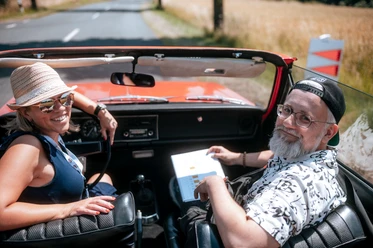 PS.Rallye 2023 Two people sitting in a red vintage car in sunny weather.