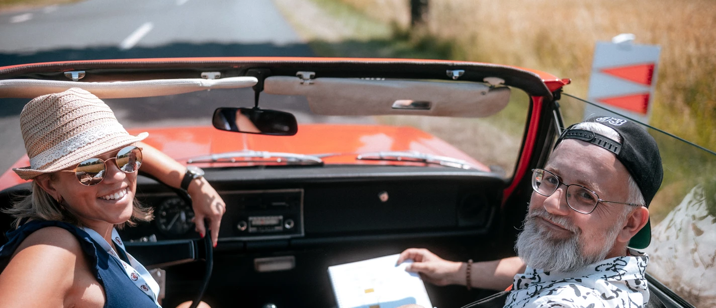 PS.Rallye 2023 Two people sitting in a red vintage car in sunny weather.