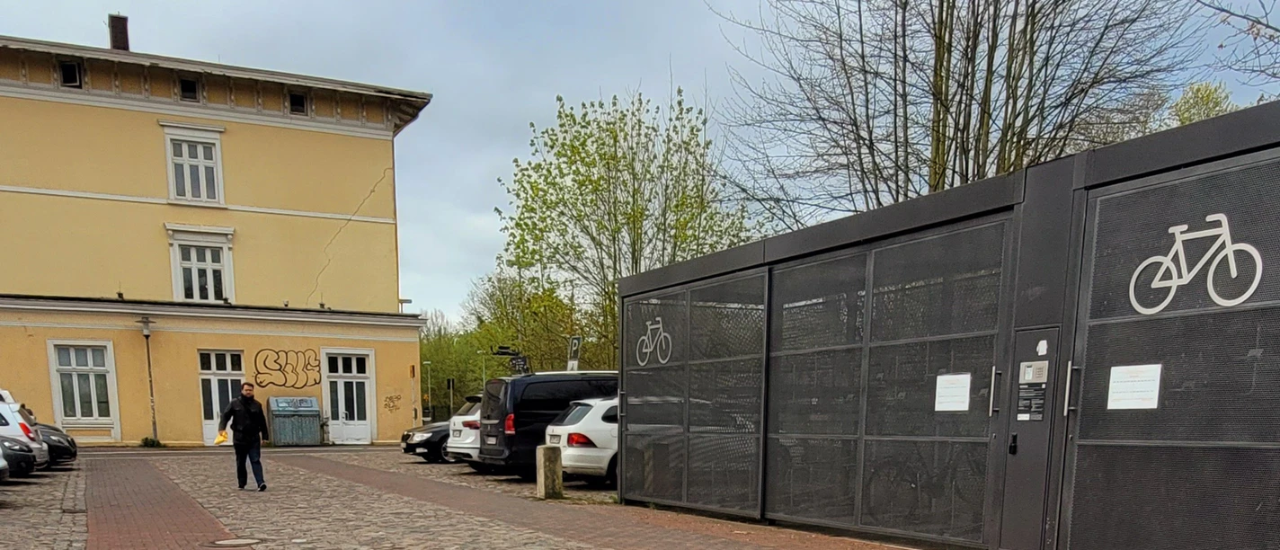 Bahnhof Ratzeburg_Silvana Dust_1980x1080_20230510 (6).jpg Hinteransicht Bahnhofsgebäude Ratzeburg mit Parkplätzen für Autos und Fahrräder