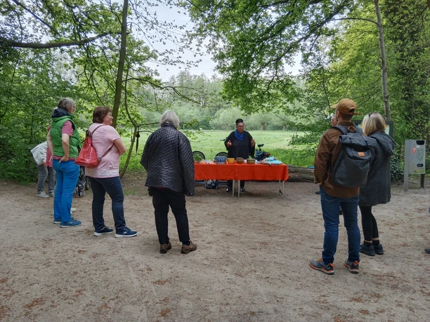 IMG_20220507_160147.jpg Eine Gruppe von Menschen lauscht einem Vortrag in einem Wald, hinter ihnen erstreckt sich eine grüne Wiese.
