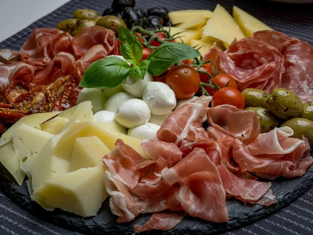 Beipielbild Ein reichhaltiges Antipasti-Arrangement mit Käse, Mozzarella, Tomaten, Schinken und Oliven auf Schiefer.