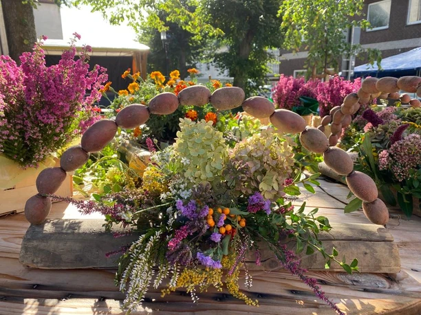 Rustikale Blumendekoration mit Kartoffelbogen und bunten Blumenarrangements auf Holztisch im Freien.