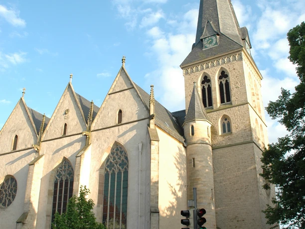 Historische Kirche mit gotischen Elementen, markantem Turm und grünen Bäumen unter blauem Himmel.