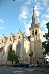 DSC_5396.JPG Historische Kirche mit gotischen Elementen, markantem Turm und grünen Bäumen unter blauem Himmel.
