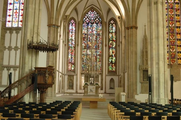 Gotische Kathedrale in Osnabrück mit beeindruckenden Buntglasfenstern und reihenweise Sitzbänken.