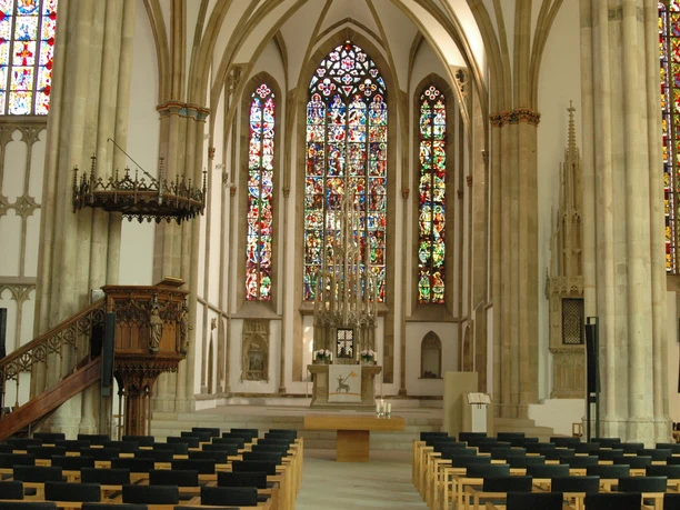 Gotische Kathedrale in Osnabrück mit beeindruckenden Buntglasfenstern und reihenweise Sitzbänken.