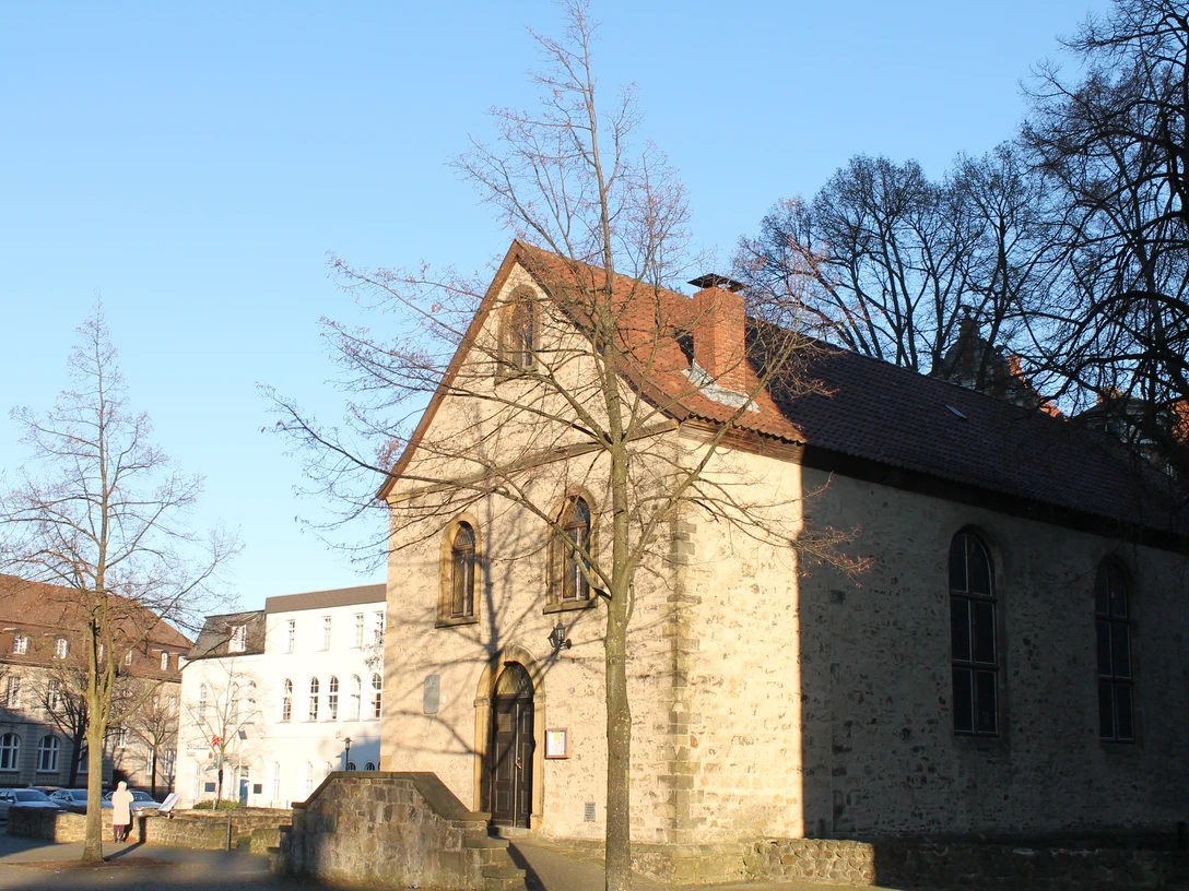 Wolderuskapelle mit hellen Natursteinen und Satteldach in einer ruhigen, urbanen Umgebung.