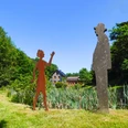 Sinneswald-Braun-Brudes.jpg Zwei Skulpturen, eine Frau und ein Mann, stehen auf einer grünen Wiese vor einem Haus im Hintergrund.