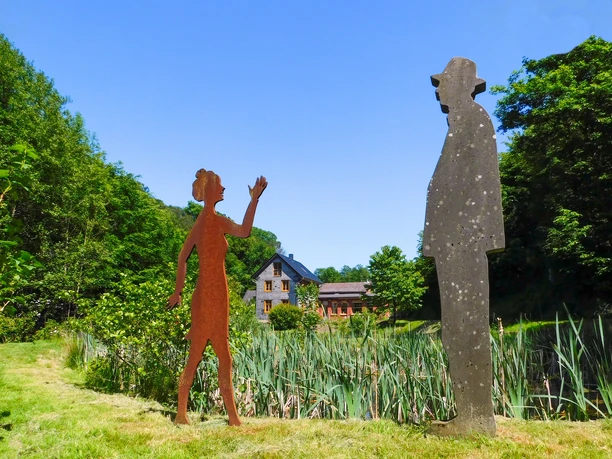 Sinneswald-Braun-Brudes.jpg Zwei Skulpturen, eine Frau und ein Mann, stehen auf einer grünen Wiese vor einem Haus im Hintergrund.