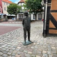 Bronzefigur eines historischen Arbeiters mit Schlägermütze auf gepflastertem Platz in Stadtkulisse.