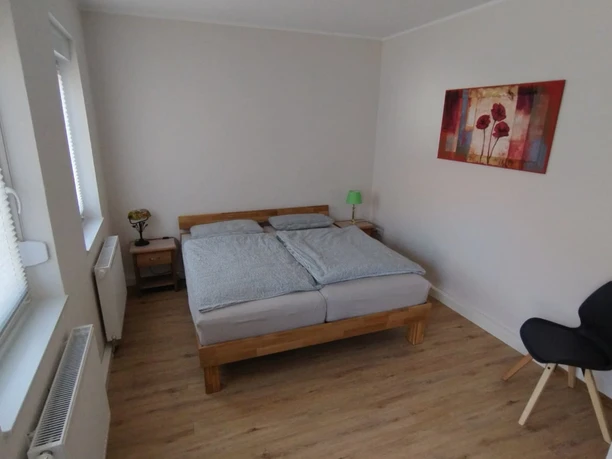 A bright bedroom with double bed, two bedside tables, chair and art picture on the wall.