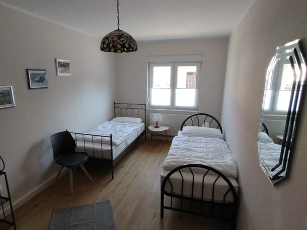 Burkis Ferienhaus Zwei Einzelbetten in einem schlichten, hellen Raum mit Parkettboden und Wandbildern, Tageslicht erhellt.