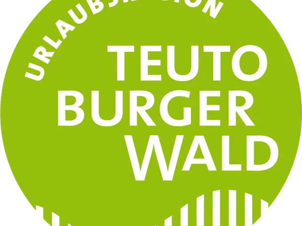 Rundes, grünes Logo mit weißem Text "Urlaubsregion Teutoburger Wald" und geschwungenen Linien.