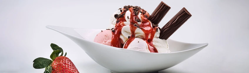 LaLuna Eine Eisschale mit Erdbeeren, Sahne, und Schokostäbchen, dekoriert mit roter Soße und Schokostreuseln.