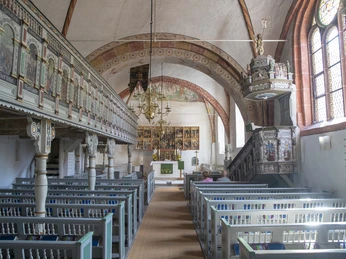 Innenraum.jpg Der Innenraum einer historischen Kirche zeigt reihenweise bemalte Holzbänke, kunstvolle Fresken und ein filigranes Chorgestühl.