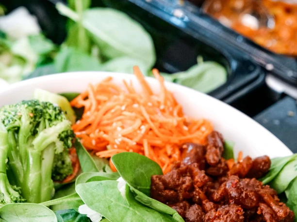 Áro Frischer Salat mit Brokkoli, Karotten und fleischähnlichen Stücken auf einem Buffet präsentiert.
