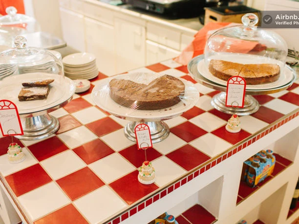 GundolfS Drei Kuchen auf roten und weißen Kacheln, umgeben von kleinen dekorativen Süßigkeiten.