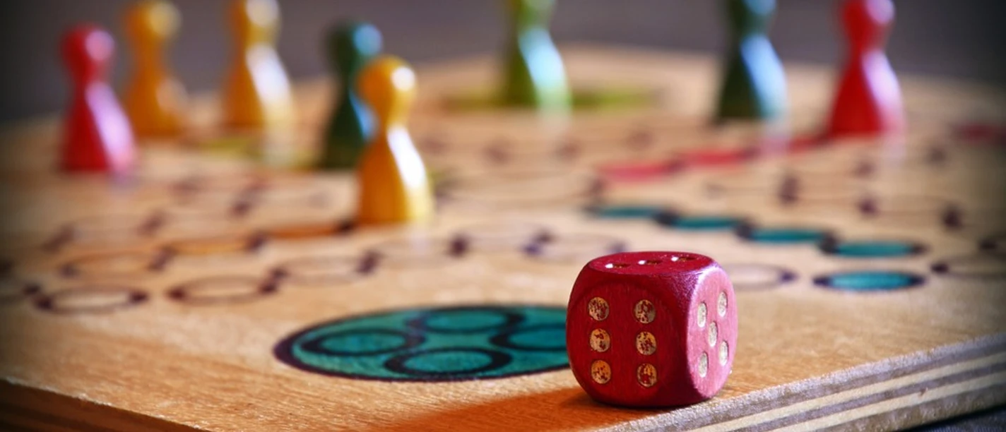 Beispielbild Holzspielbrett mit würfel und bunten Spielfiguren, ein Symbol für geselliges Beisammensein.