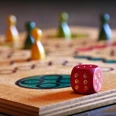 Voorbeeldafbeelding Holzspielbrett mit würfel und bunten Spielfiguren, ein Symbol für geselliges Beisammensein.Wooden game board with dice and colorful game pieces, a symbol for social get-togethers.Spilleplade af træ med terninger og farverige brikker, et symbol på socialt samvær.Houten speelbord met dobbelstenen en kleurrijke speelstukken, een symbool voor sociale bijeenkomsten.