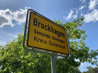Brockhagen.jpeg Ortsschild von Brockhagen, Gemeinde Steinhagen, Kreis Gütersloh, vor grünen Bäumen und blauem Himmel.