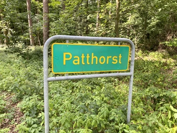 Ortsschild von Patthorst im Wald, umgeben von üppigem Grün und dichten Bäumen.