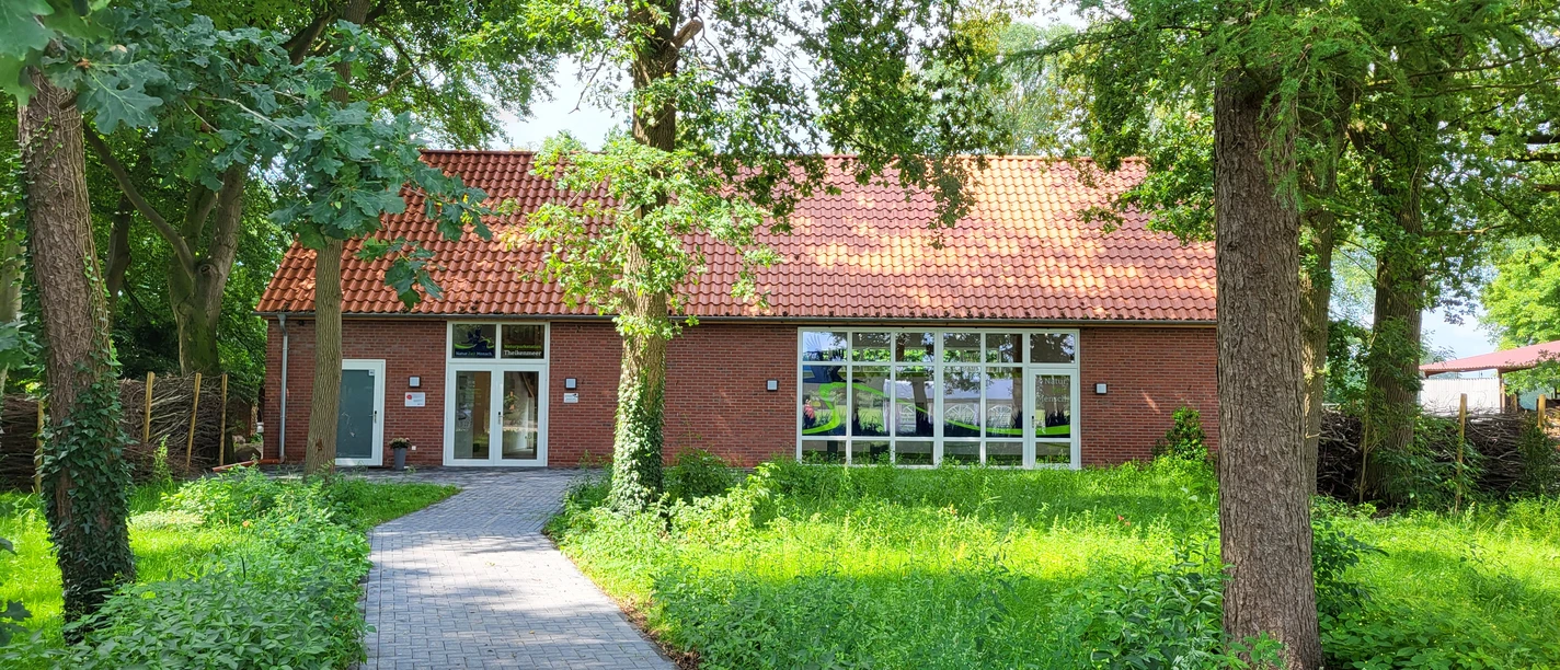 Theikenmeer-Runde, Werlte - Hümmling-Pfade, Naturparkstation ©Naturpark Hümmling (3).jpg Backsteingebäude mit rotem Ziegeldach, umgeben von Bäumen und begrüntem Weg zur Eingangstür.