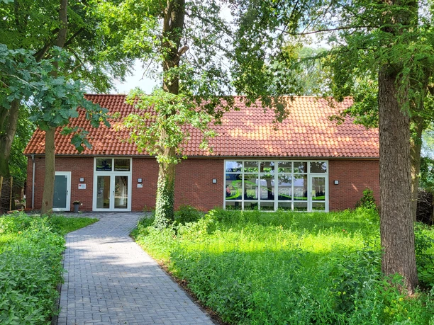 Theikenmeer-Runde, Werlte - Hümmling-Pfade, Naturparkstation ©Naturpark Hümmling (3).jpg Backsteingebäude mit rotem Ziegeldach, umgeben von Bäumen und begrüntem Weg zur Eingangstür.
