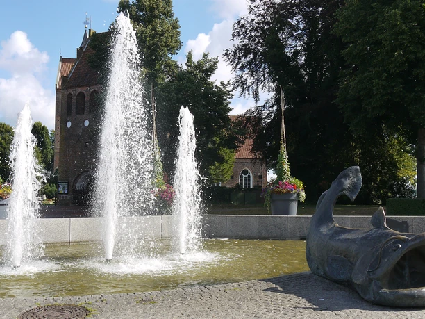 zwischenahner-wels-brunnen-marktplatz.jpg Springbrunnen mit Wels-Skulptur auf dem Marktplatz Bad Zwischenahn vor der St. Johannes-Kirche.