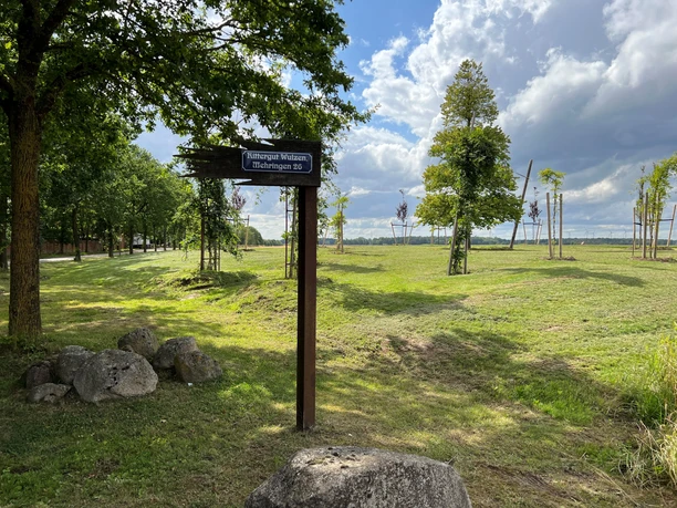 Rittergut Wulzen Ein Wanderweg-Schild und Felder unter bewölktem Himmel; eine Mischung aus Natur und Wegweiser.