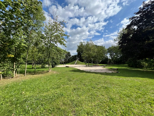 Rittergut Wulzen Grüne Wiese mit Spielplatz unter blauem Himmel, umgeben von Bäumen, entspannter Ort für Erholung.