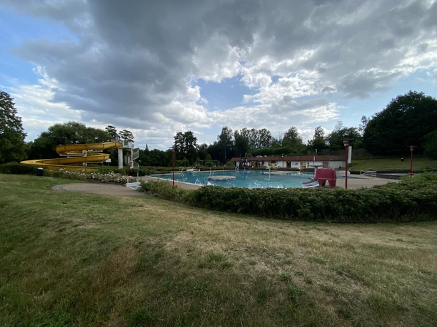 Outdoor pool Rathewalde An outdoor pool with a yellow water slide, a large pool and a red elephant slide, surrounded by grass and trees under a cloudy sky.