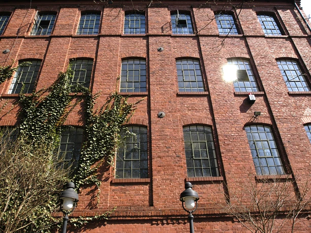 Fassade eines Backsteingebäudes mit vertikalem Efeubewuchs und vielen Sprossenfenstern.