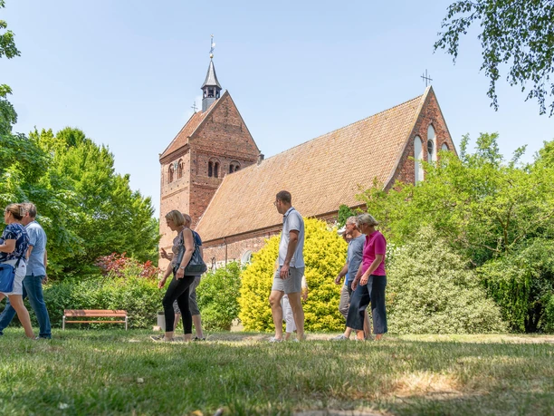 sehenswürdigkeiten.jpg Vor einem Backsteingebäude ragt der Kirchturm auf, während Menschen auf dem grünen Rasen spazieren.