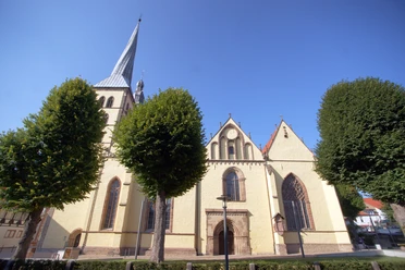 Kirche St. Nicolai Die Kirche St. Nicolai in Lemgo mit imposantem Turm ist von Bäumen umgeben und bei blauem Himmel sichtbar.