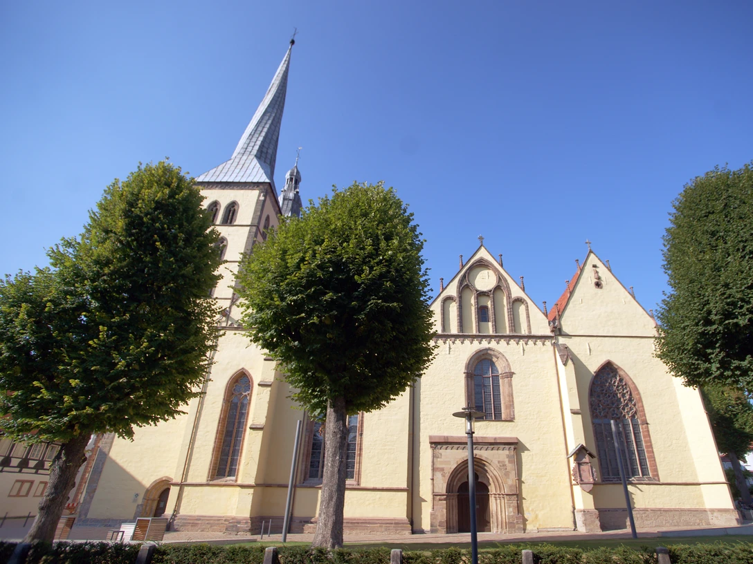 Kirche St. Nicolai Die Kirche St. Nicolai in Lemgo mit imposantem Turm ist von Bäumen umgeben und bei blauem Himmel sichtbar.