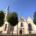 Kirche St. Nicolai Die Kirche St. Nicolai in Lemgo mit imposantem Turm ist von Bäumen umgeben und bei blauem Himmel sichtbar.